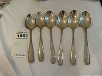 Full set of six spoons laid side by side showing monogram placement and general condition