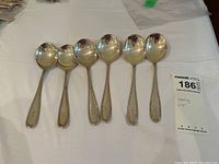 Six silver spoons arranged on a white surface with lot tag visible