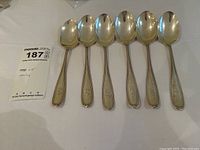 Six sterling silver monogrammed spoons laid in a row, showing front views with handles and bowls visible.