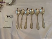 Set of six sterling silver monogrammed teaspoons laid out side by side showing overall condition and tarnishing.