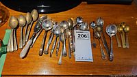 Overview of assorted demitasse spoons and forks laid out on wood surface with MaxSold lot tag visible.
