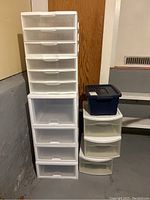Tall white Sterilite plastic drawer storage unit with multiple drawers and two shorter white storage units with drawers beside a Rubbermaid blue bin on top.