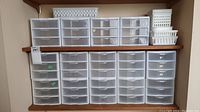 Two shelves filled with clear plastic drawer units and white baskets for small storage.