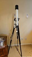 Full view of the white telescope mounted on a black-adjustable wooden tripod.