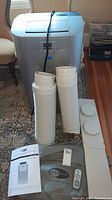 Full view of the Whynter portable air conditioner unit with hoses, vent panel, instruction manual, remote, and storage cover
