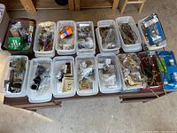 Top-down overview of 14 bins filled with assorted hardware, plumbing parts, and fasteners on a wooden desk surface.