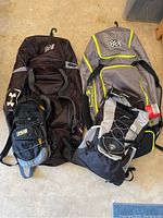All four bags shown together on floor including 2 large Under Armour baseball bat bags and smaller backpacks