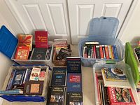 Three blue plastic bins filled with assorted books on medicine, anesthesiology, self-help, cooking, and science with some books stacked outside the bins.