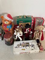 Overview of multiple Christmas decorations and figurines including a large bear, dolls, and boxed ornaments