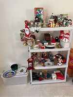 Wide shot of white metal shelving unit holding assorted Christmas decorations with a white storage bin on the floor.