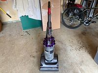 Front-facing photo of Dyson DC17 Animal vacuum in garage showing full vacuum upright with clear dust canister, purple cyclone design, and red handle.