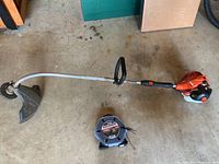 Full view of Echo gas trimmer with curved shaft, loop handle, orange engine housing, and protective guard near cutting head, placed on concrete.