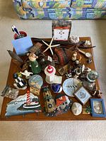 Overview photo showing entire lot of nautical and coastal figurines and wall decorations on a table, including lighthouses, starfish, and various small knickknacks