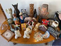 Full assortment of ceramic and wood figurines on oval wood table, including animal and human figures, decorative plates, and other knickknacks.