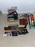 Full view of the lot containing plastic bin with games and DVDs, backgammon board, water launchers, toy vehicles, and a box for a traffic light game toy.