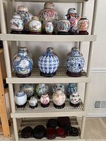 Full display shelf with three levels containing assorted ginger jars of various sizes, patterns, and colors, all on wooden bases, plus extra loose bases on bottom shelf.