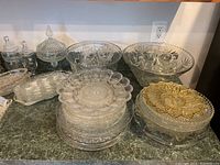 Overview of clear glass serving bowls, plates, and condiment containers with lids arranged on counter.