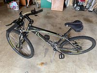 Side angle view of the black Raleigh mountain bike showing frame, tires, seat, and pedals indoors on concrete floor.