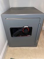 Closed gray Sentry combination safe with black and red dial and handle on the front.