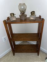 Straight front view of the three-tier wooden shelf with clear wood grain. Shelf is empty except for glass items shown for scale, but not included in sale.