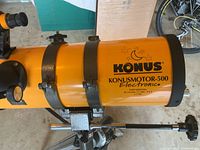 Side close-up of the Konusmotor 500 Newtonian telescope tube mounted on bracket, showing orange tube and Konus branding.