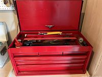 Open tool box showing top compartment with assorted tools such as pliers, screwdriver, and coiled spring component.