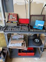 Full view of metal utility shelf loaded with assorted tools, air filters in packaging, two wheels, and red toolbox on lower shelf.