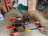 Full lot image showing Black & Decker Edge Hog edger with red wheels, several Black & Decker tools and battery packs neatly arranged on garage floor, Craftsman chainsaw visible.