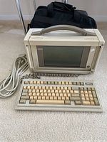 Front angle of vintage Compaq portable computer with keyboard and carrying case visible