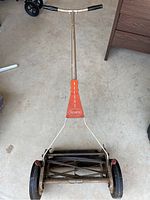 Full view of vintage manual reel lawn mower showing handle, wheels, and cutting reel on concrete floor.