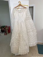 Vintage white lace wedding dress hanging on a yellow hanger, showing the front side with long lace sleeves and detailed floral patterns.
