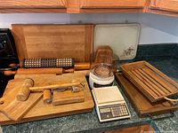 Overview photo showing all wooden kitchen items including cutting boards, rolling pins, mallets, napkin holder, food processor, and scale arranged on kitchen counter.