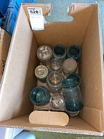 Top view of box showing twelve Ball mason jars with some metal lids and some without lids, all blue-green tinted glass.