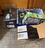 Three boxes containing assorted Ball and Mason jars, some jars visible with lids and packaging inside plastic containers and cardboard boxes.