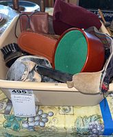Photo showing a tub containing various items including binoculars case, wallets, camera, shoe brush, ties, and small accessories.