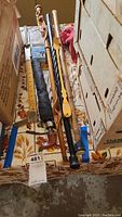 Photo showing several canes, umbrella, wooden ruler, and back scratcher arranged horizontally on a floral table cover among cardboard boxes.