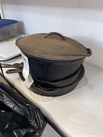 Stacked large cast iron pot with lid on top of other pans on a table