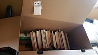 Photo of a box filled with multiple vintage cookbooks viewed from above, showing the spines and bindings of around 13 books.