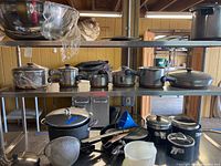 Shelf with large mixing bowls wrapped in plastic and a line of pots and pans with handles and lids, alongside a frying pan.