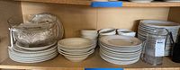 Shelf with stacks of white ceramic plates and bowls, clear glass bowls on the left