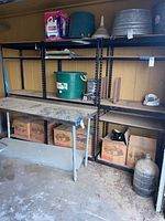 Four black metal shelving units shown against a wall with various items on and around them. Older condition with visible dirt and wear.