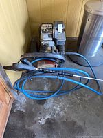 Front view of Pacific Hydrostar pressure washer showing engine, frame, and coiled blue hose with spray wand.