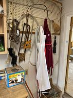Lot contents showing hanging handsaws, aprons, electrical cords, brush, and boxed household pump on shelf
