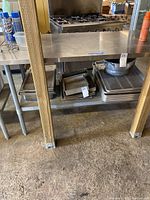 View of metal utility table with stainless steel surface and lower shelf, showing legs and floor below.