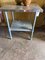 Front view of metal utility table showing stainless steel top, metal tubular legs, and lower shelf.