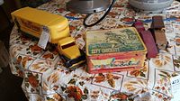 Vintage Davy Crockett lunch box, yellow metal and wood toy truck, and two wooden toy trucks on a floral tablecloth.