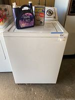 Front view of white top load washing machine with supplies on top