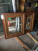 Pair of matching antique mirrors with wood and ornate gold frames leaning against a wall.