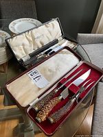 Two vintage carving sets in boxes, showing one with cream satin lining and the other with white satin lining, both with stag horn handled knives and forks.