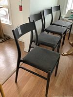 Four of the six black chairs displayed in a row on hardwood floor.